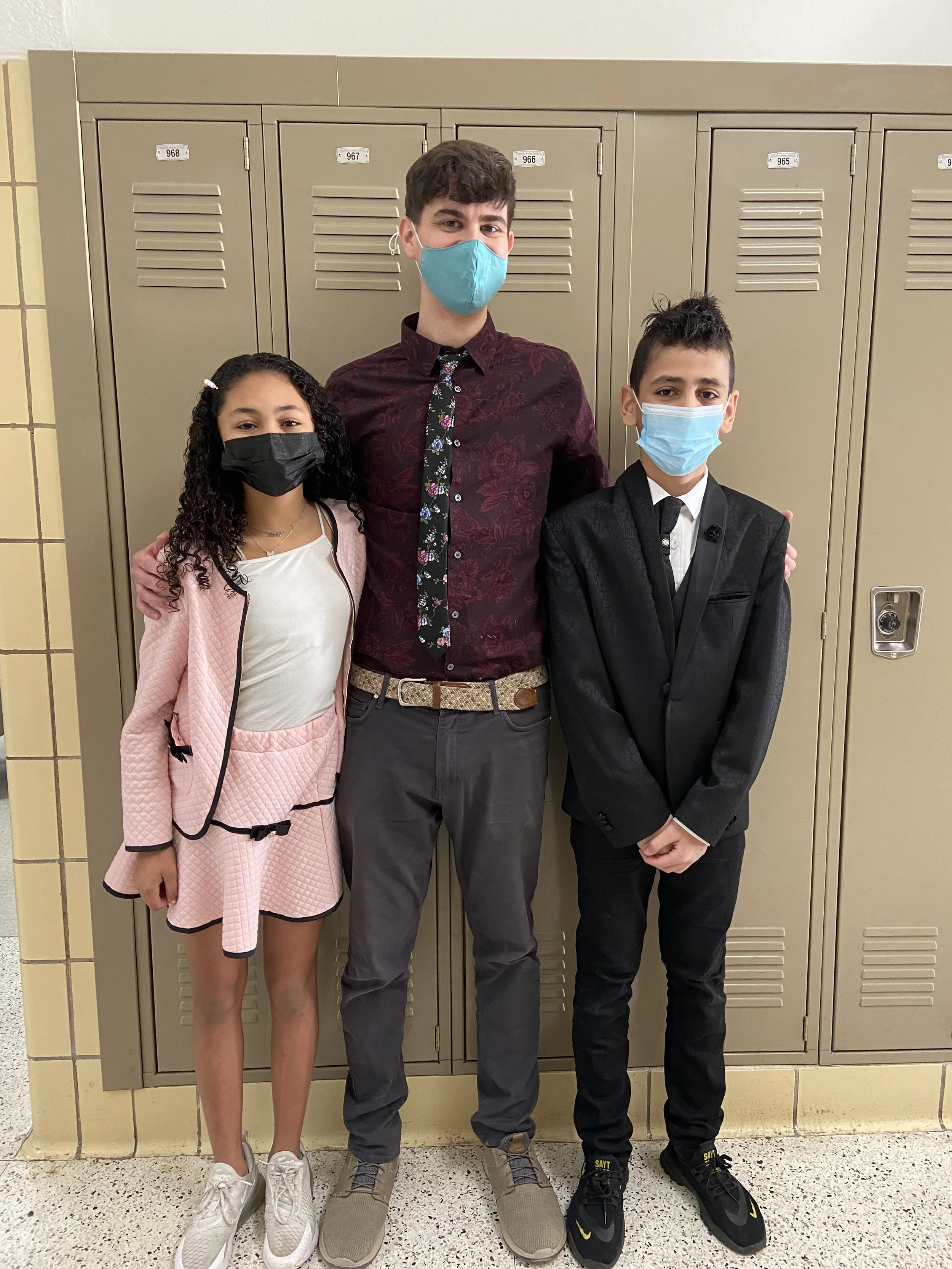 Three people wearing face masks standing in front of school lockers.