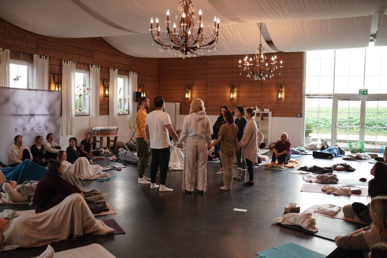 Teilnehmer*innen stehen im Kreis während einer Gruppen-Session im warm beleuchteten SPACE Studio mit Yogamatten und ruhiger Atmosphäre