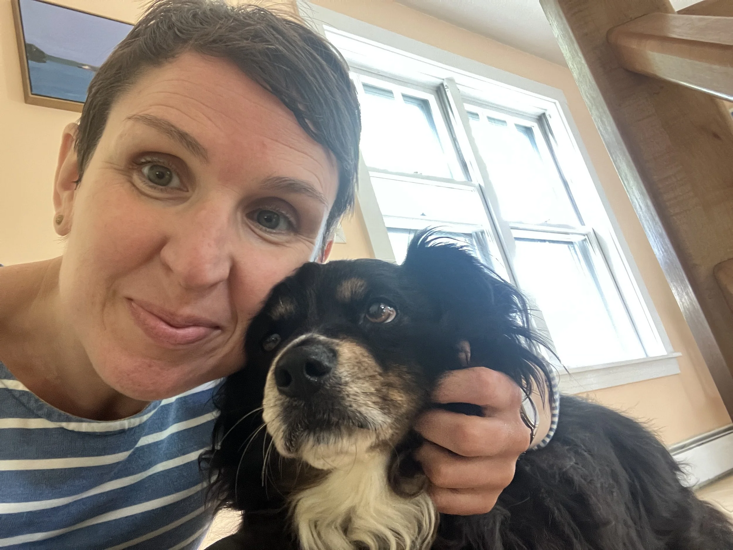 Woman wearing striped shirt with her hand around a black and white dog next to her.