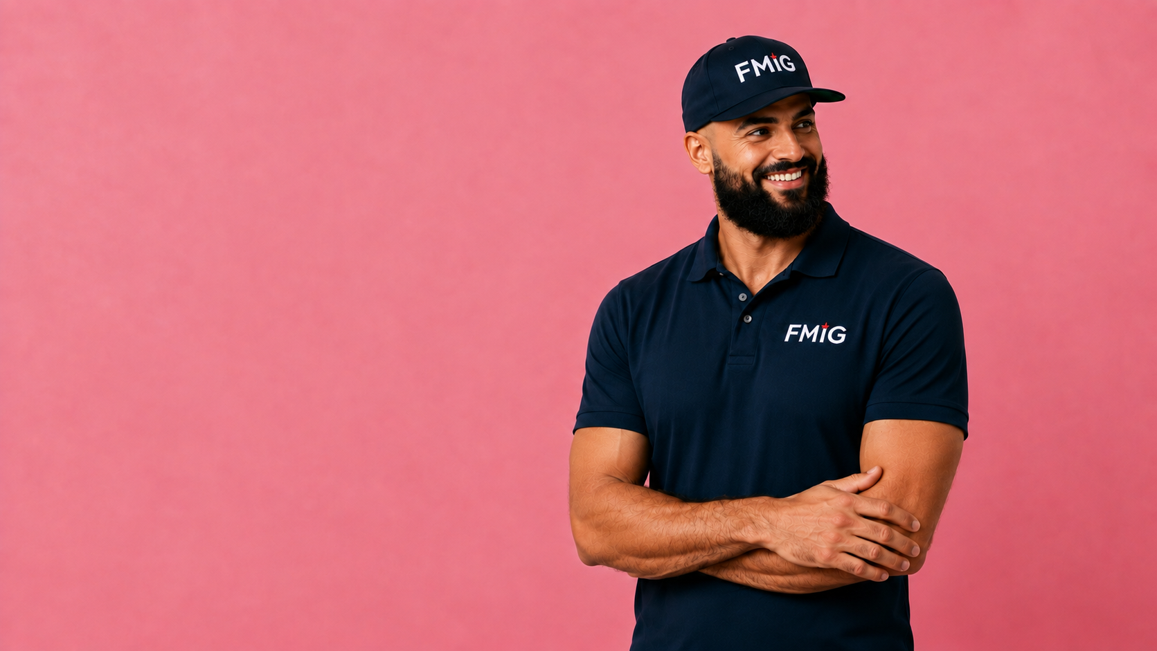 A smiling man with a beard wearing a navy blue polo shirt and a matching navy cap, both with 'FMG' logos, standing against a pink background.