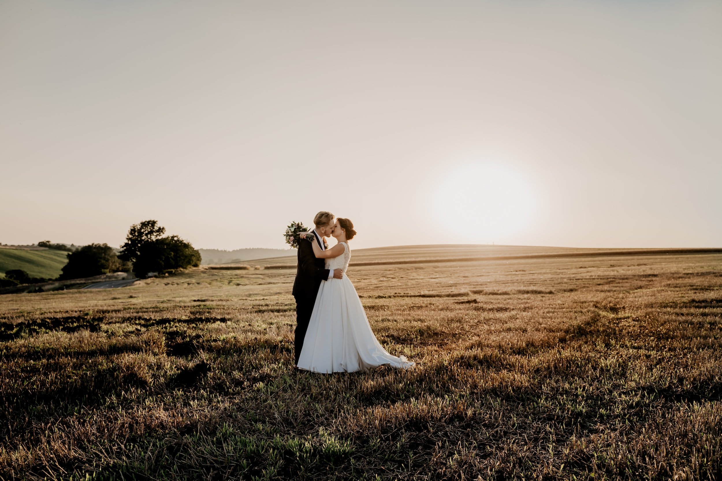 Bride and groom kissing in a field with a sunset in the background.