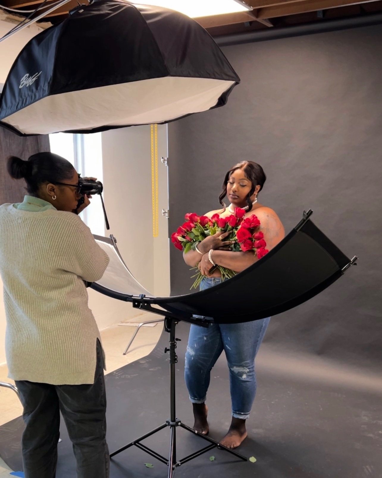 A photographer taking a picture of a woman holding a bouquet of red roses in a photo studio with professional lighting equipment.
