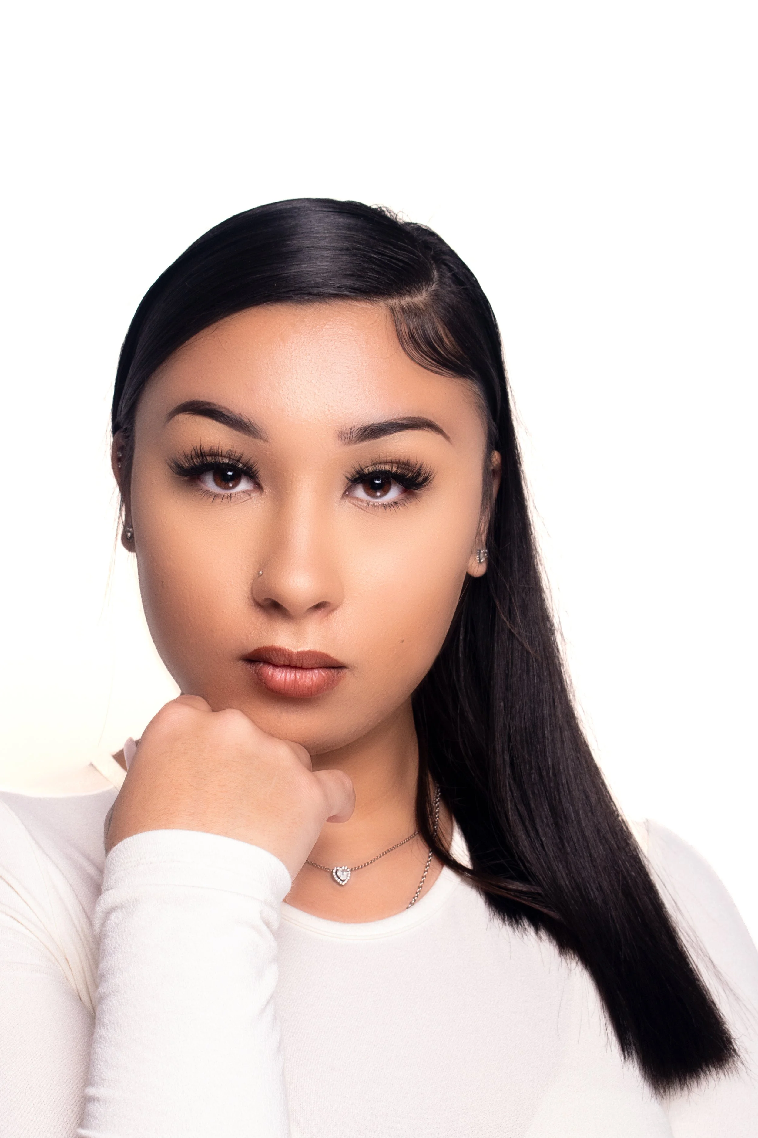 Portrait of woman with long dark hair, white shirt, wearing a silver necklace, looking forward with serious expression.