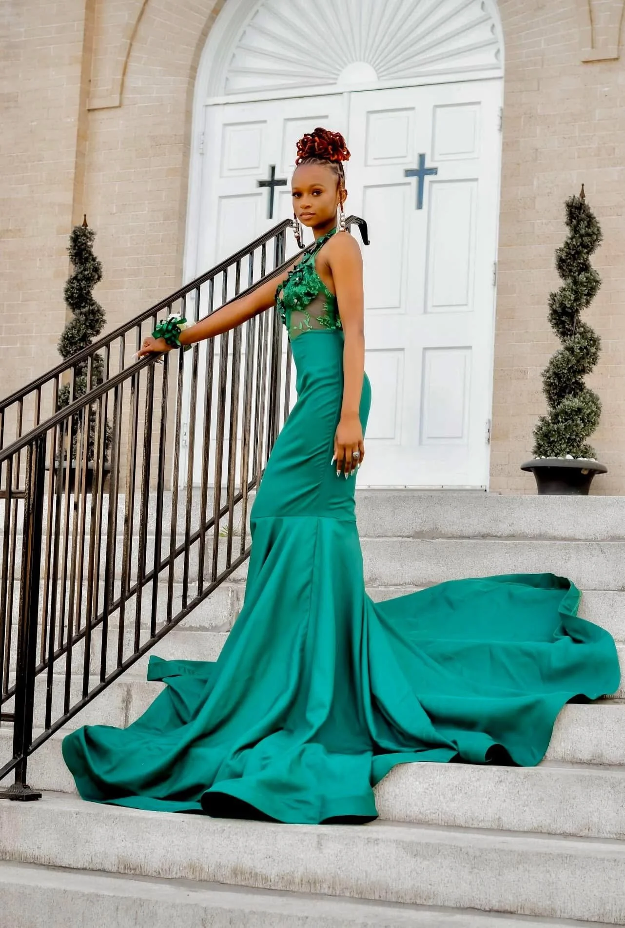 Woman in an elegant green dress standing on stairs outside a church with white doors and cross decorations.