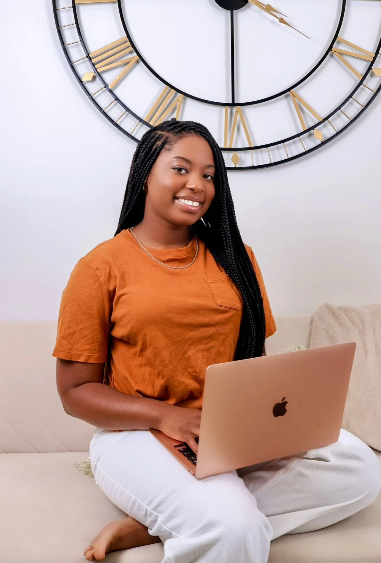 Person seated on a couch with a laptop, large wall clock in background.