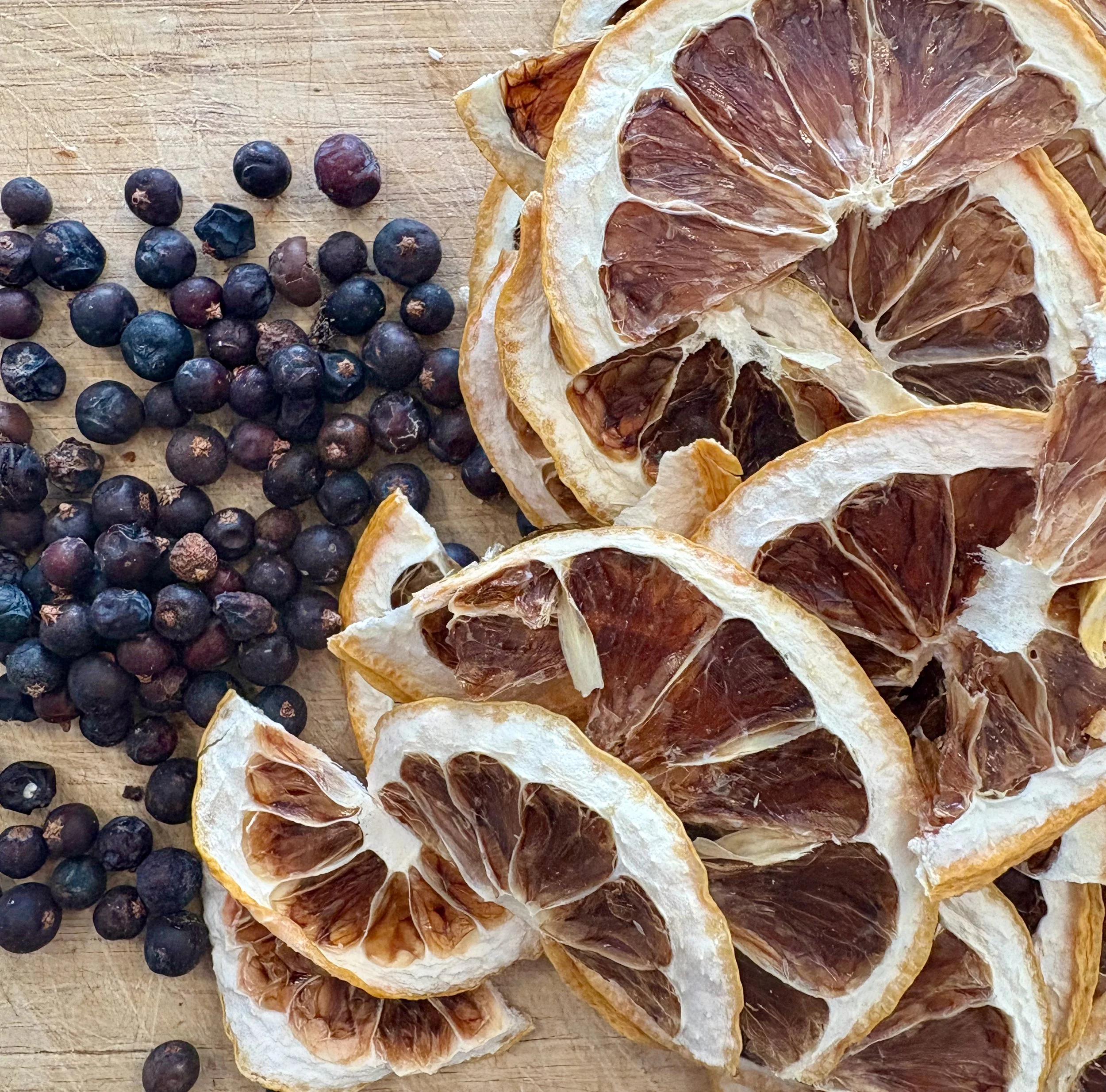 Slices of dried grapefruit and clusters of dried blueberries on a wooden surface.