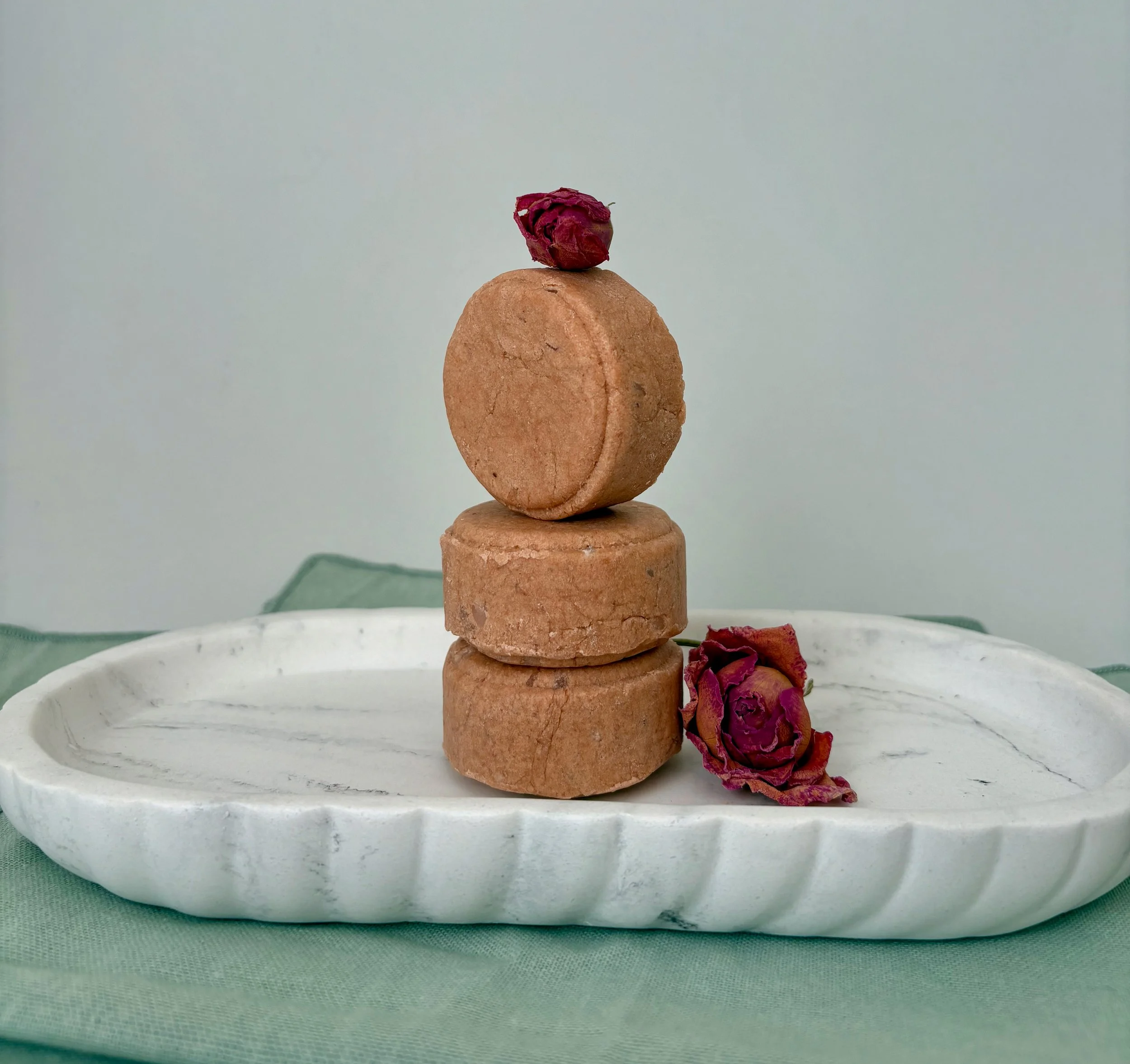 Stacked cookies with dried rose petals on top and next to the bottom layer, placed on a white plate with a mint green tablecloth.