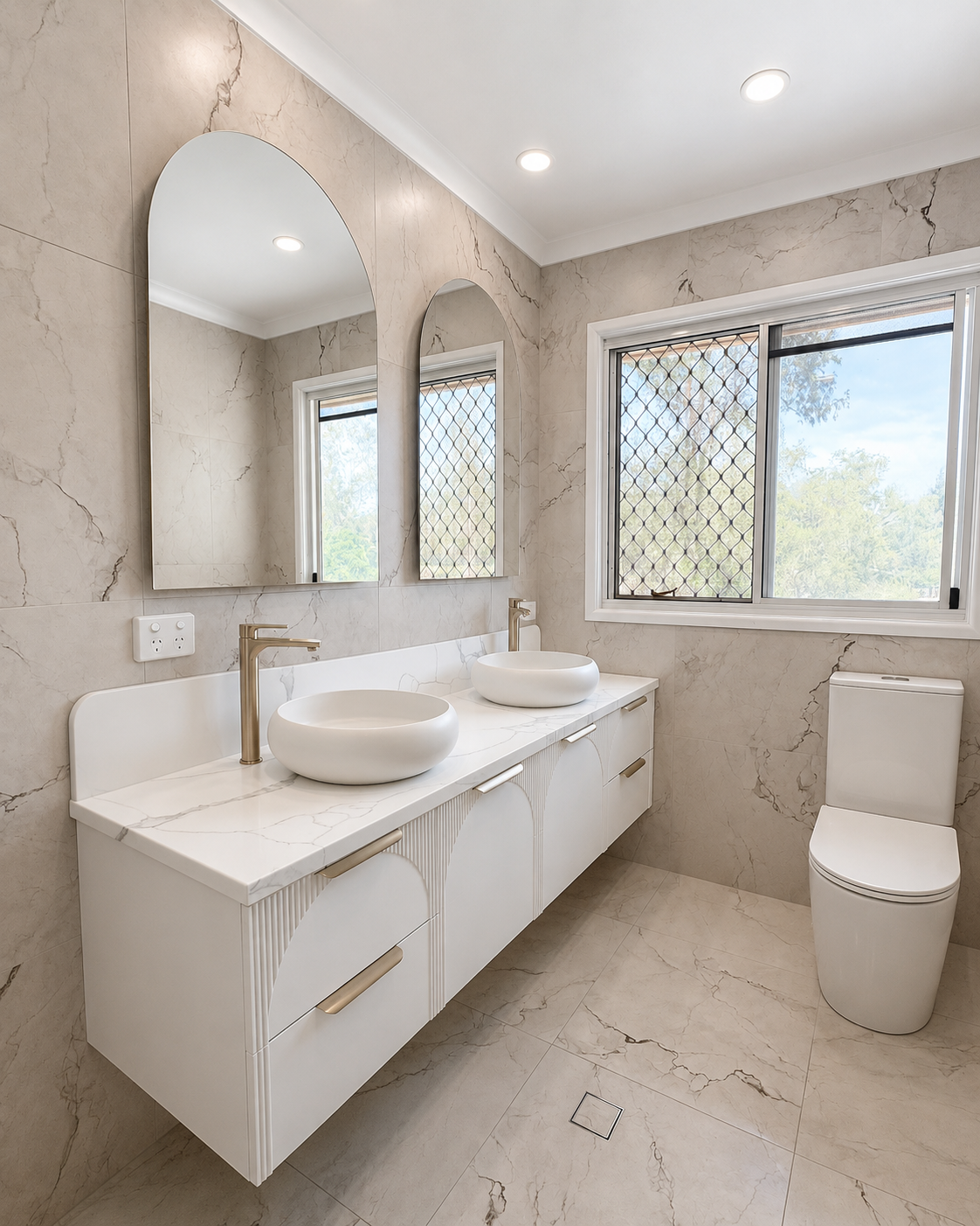Modern bathroom with marble walls and floor, double vessel sinks on a white vanity, large mirrors, a window with security grille, and a toilet.