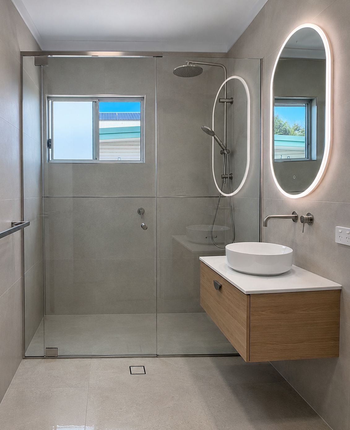 Modern bathroom with a glass shower enclosure, a window, a wall-mounted mirror with a light, a white vessel sink on a wooden vanity, and neutral-colored tiles.