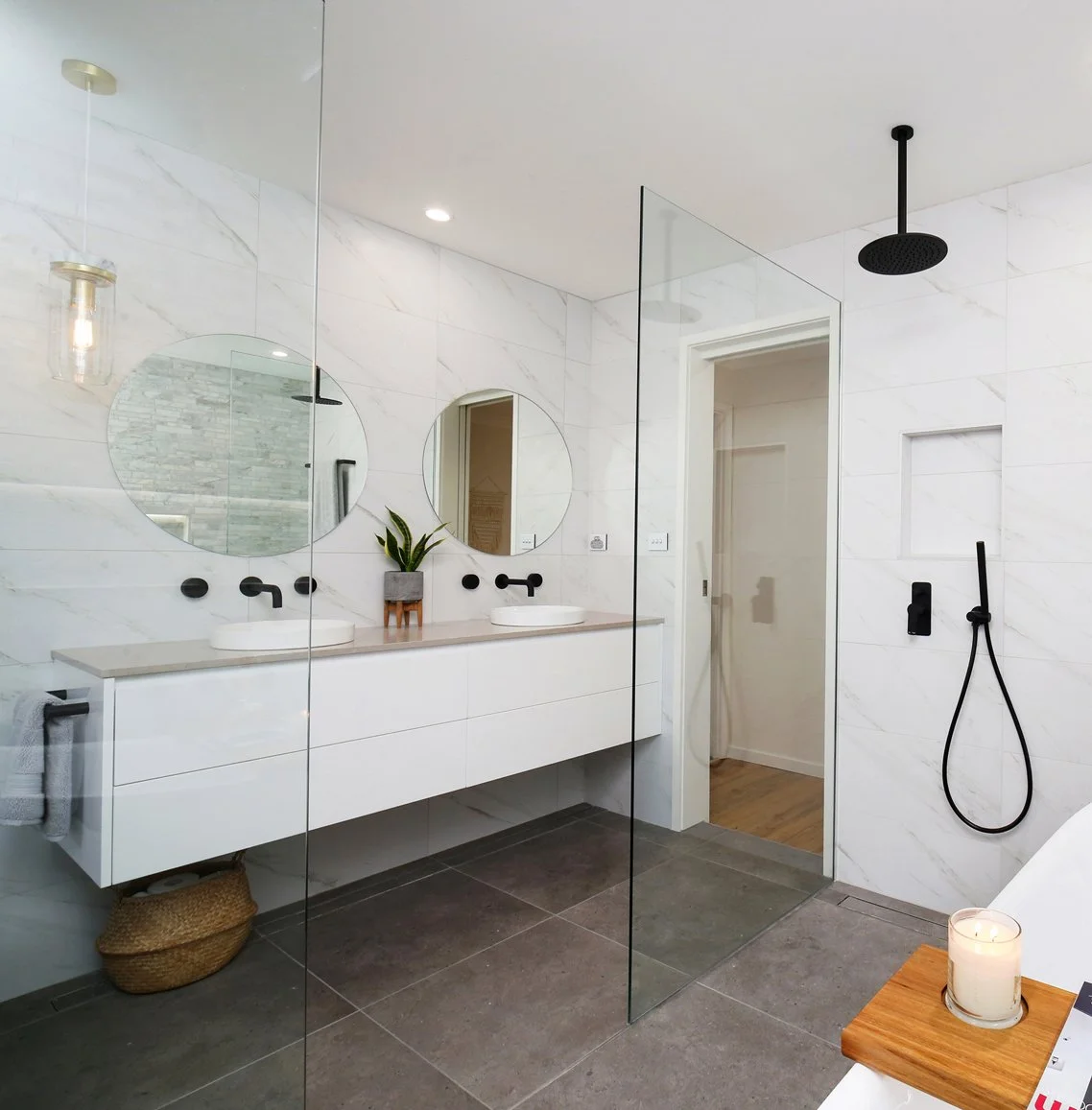 Modern white bathroom with double sinks, circular mirrors, and a walk-in shower with black fixtures, on gray tile floor and white marble walls.