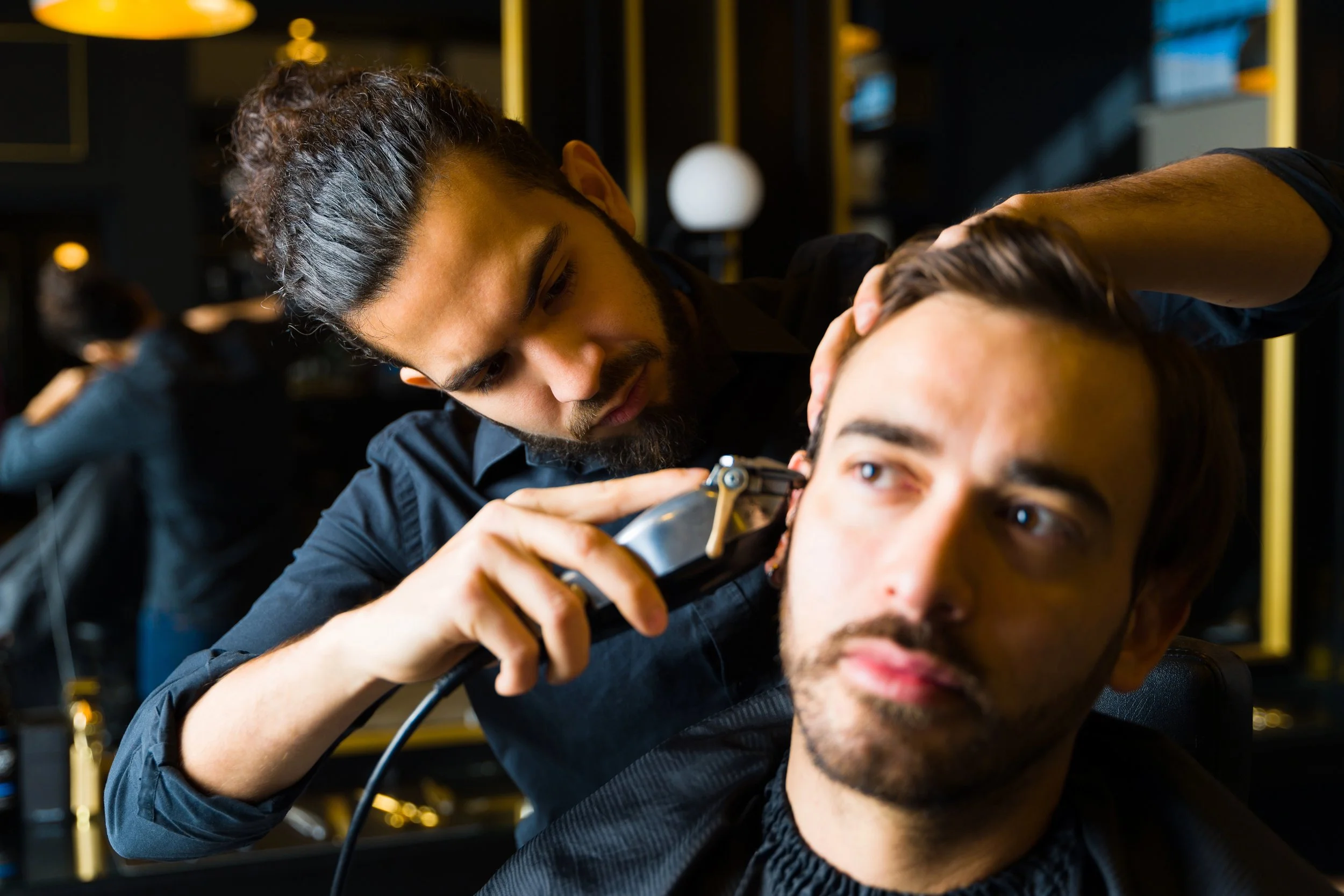 Latino/Hispanic barber uses clippers to line up client's hair