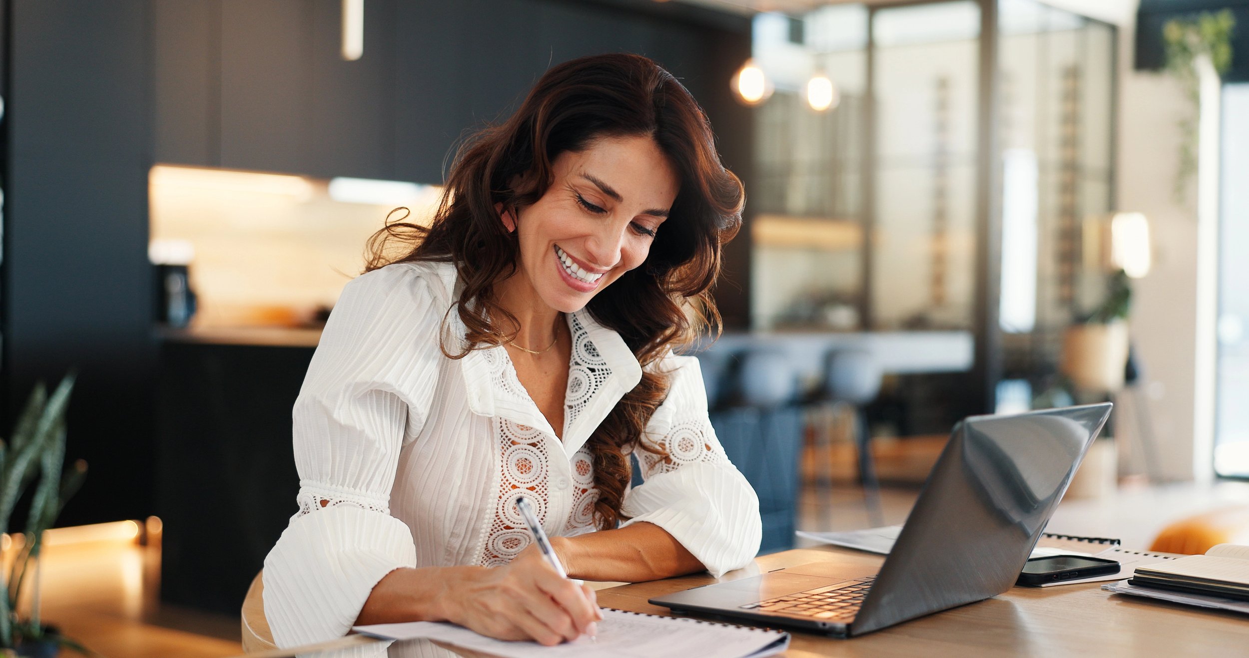 Smiling freelancer sitting in front of computer and writing in a notebook