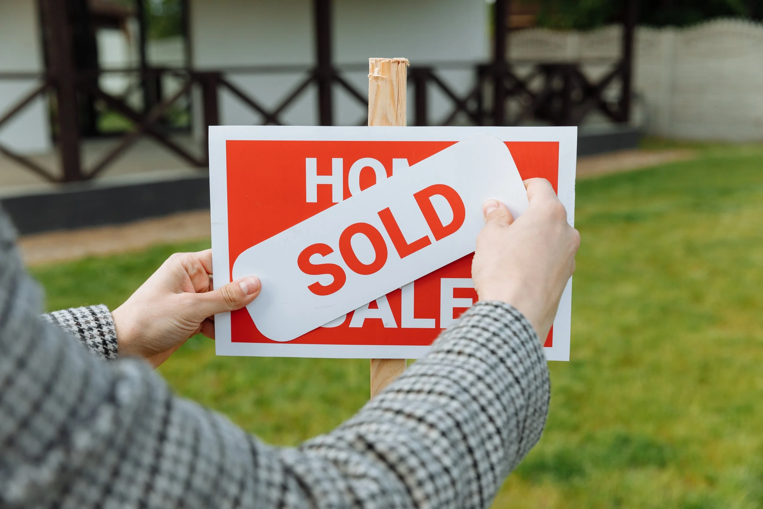 REALTOR adding sold sticker to cover for sale sign in front of a home