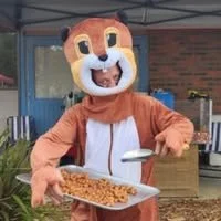 Person in a lion costume holding a tray of food outside a building.