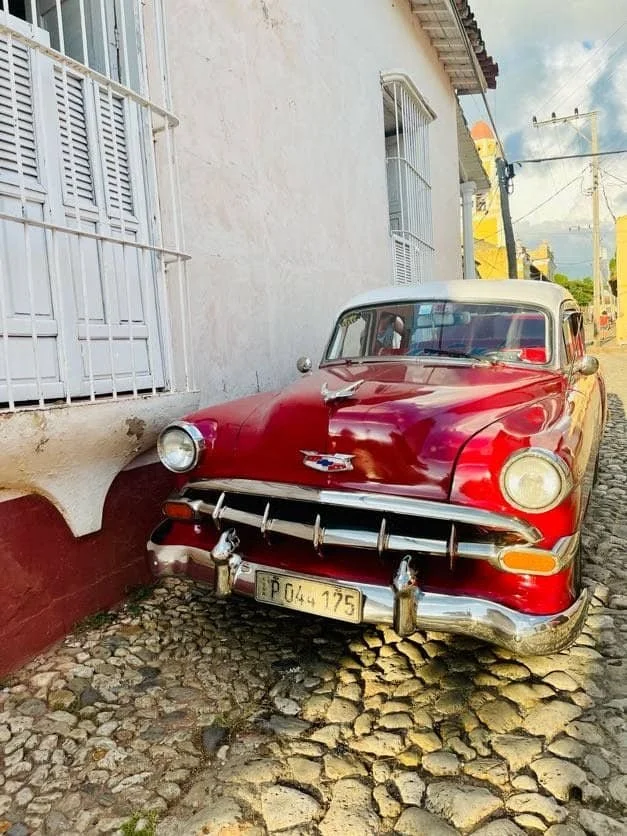 A vintage red Chevrolet parked beside a white building on a cobbled street.