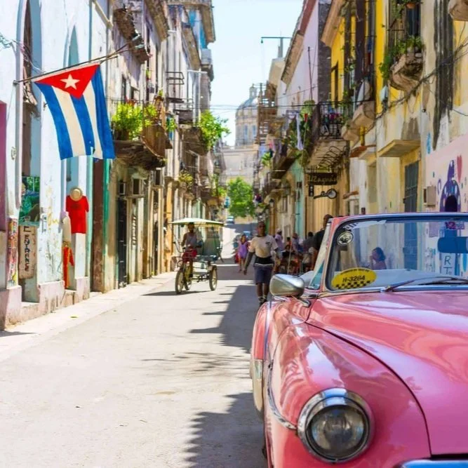 Pink car on a busy street in Havana with a Cuban flag