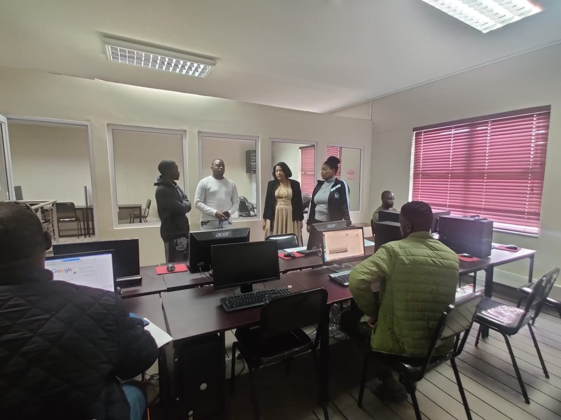 A group of people in a classroom with computers on desks and some standing.