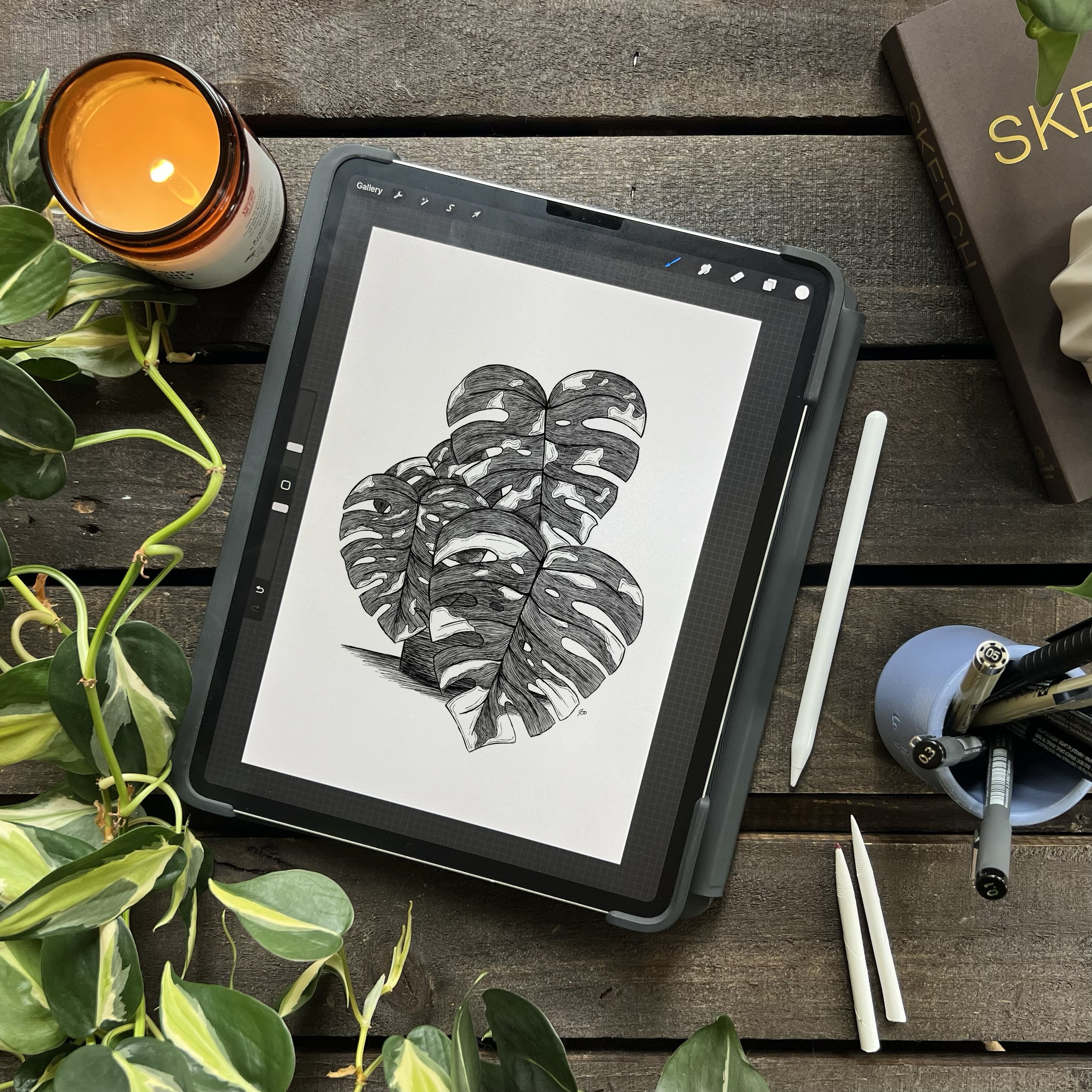 birdseye view of ipad with digital drawing of emmie the thai monstera. Plants, candle and apple pencil on table around device.