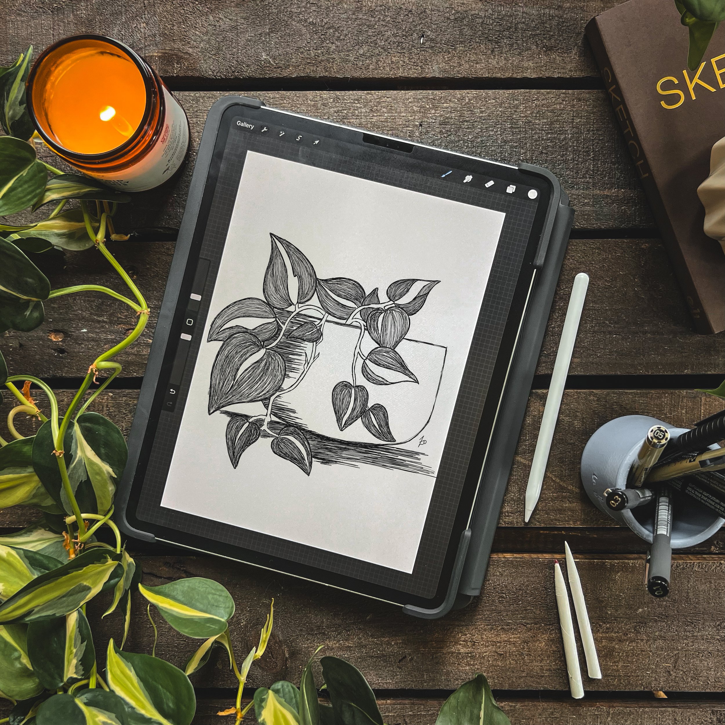 birdseye view of ipad with digital drawing of Felix the heartleaf philodendron. Plants, candle, and apple pencil on the table around device.