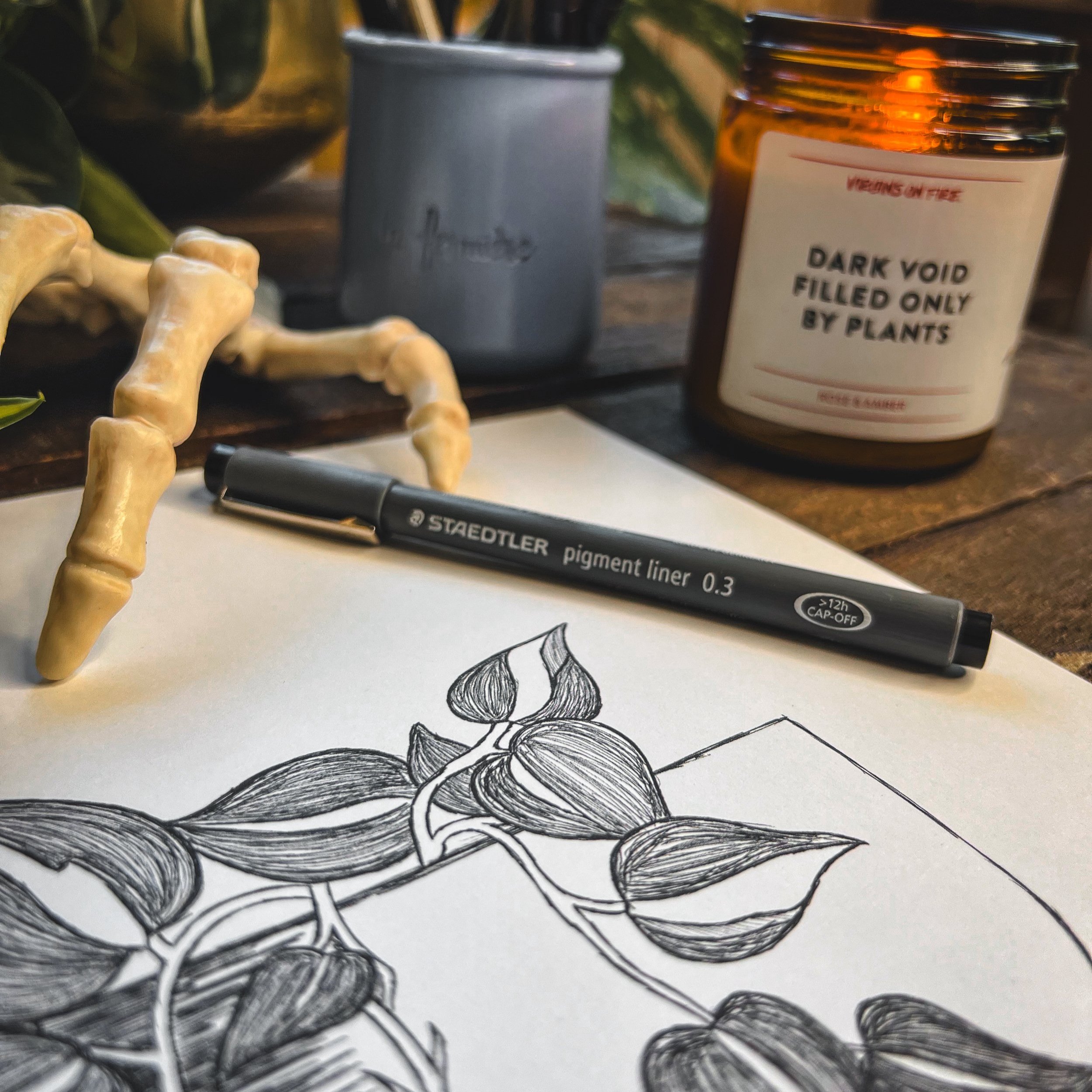 Final print of Felix the heartleaf philodendron with ink pen, candle, leaves and skeleton hand next to it on dark wooden background.