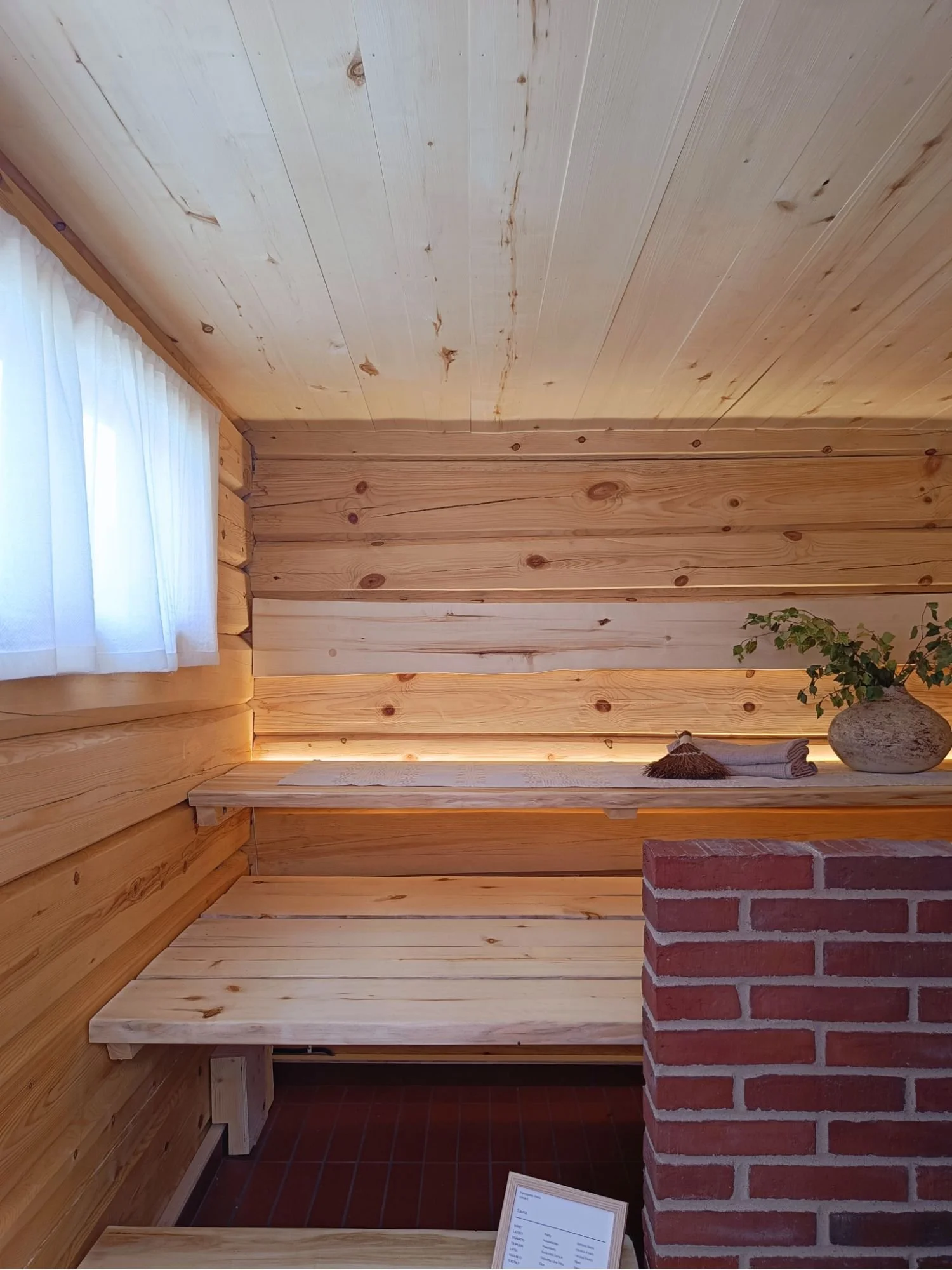 Sauna, jossa vaaleat lauteet ja punatiilinen muuri