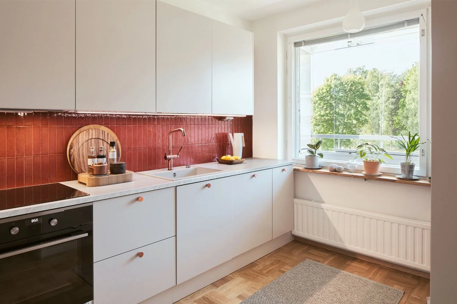 Asunnon keittiö, jossa vaaleat kaapistot ja punainen laatta välitilassa