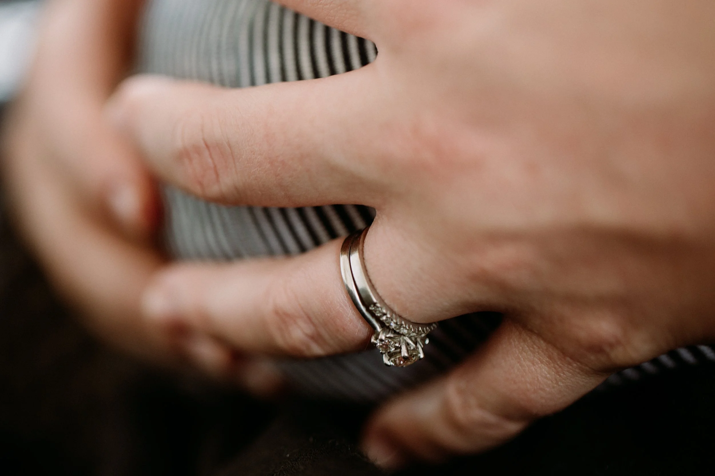 Close-up of a hand with a silver engagement ring with a large gemstone, resting on fabric with black and white stripes.