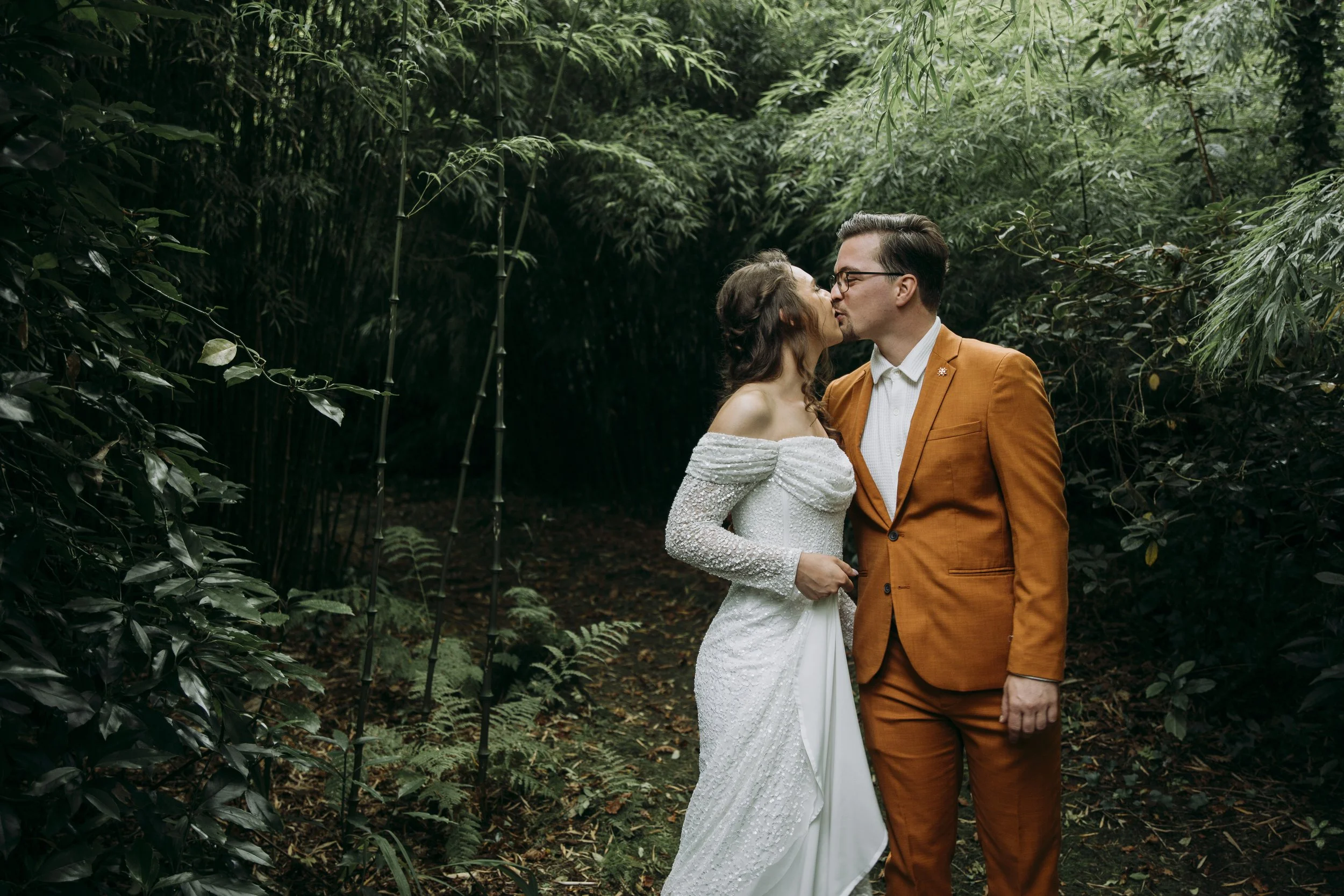 A couple in wedding attire sharing a kiss in a lush, green forest. Inish Beg - west cork
