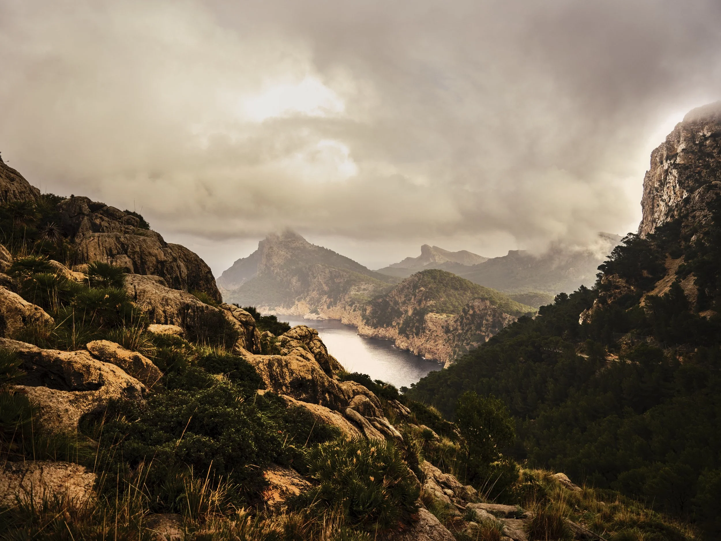Uitzicht op een berglandschap met rotsen, bomen, een meer en bewolkte hemel gefotografeerd door Eric van den Elsen in Mallorca.