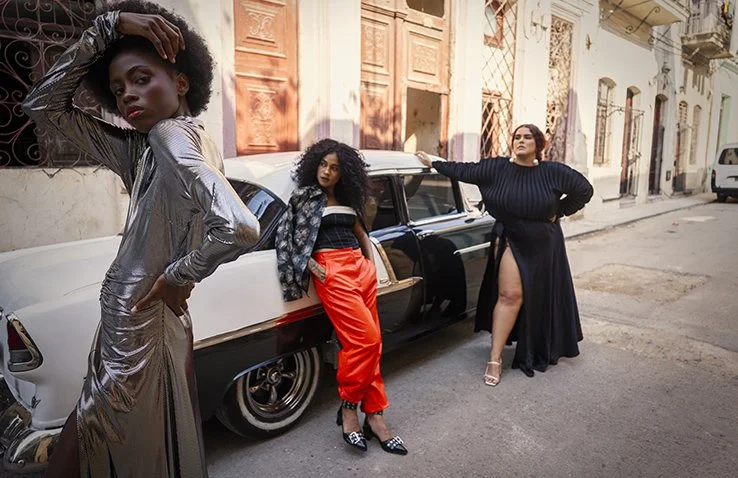 Drie vrouwen poseren op een straat naast een klassieke auto in het kleurrijk stadscentrum van Havana gefotografeerd door Eric van den Elsen.