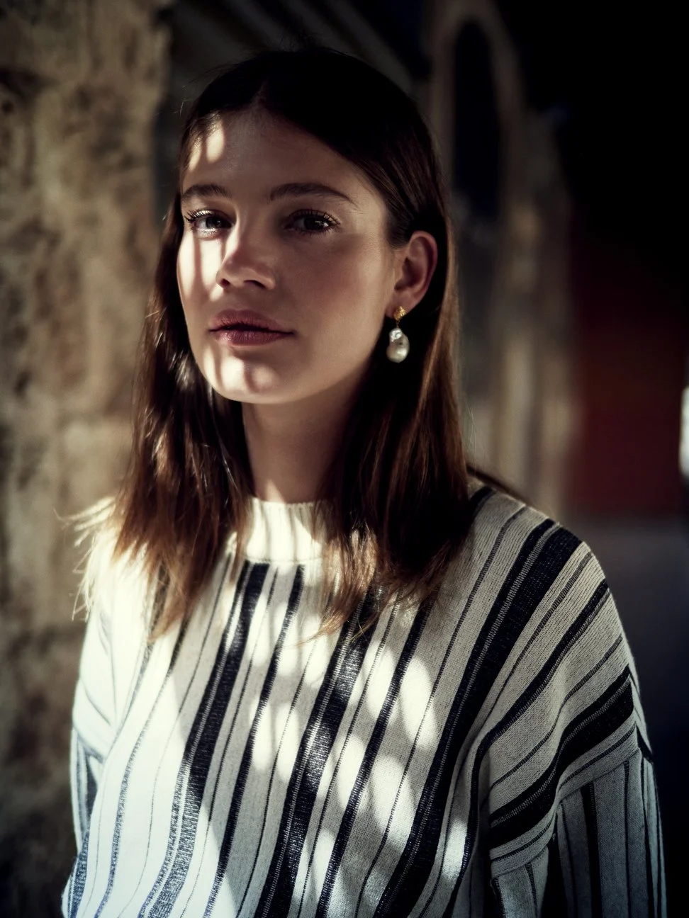 Een jonge vrouw met bruin haar en een parel oorbel, zittend binnen met lichte en donkere schaduwen op haar gezicht gefotografeerd door Eric van den Elsen.