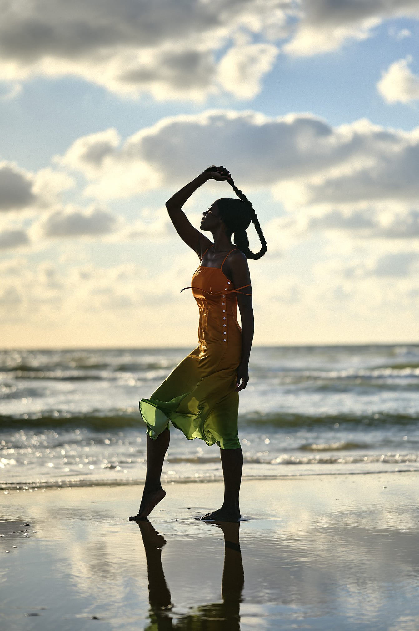 Silhouet van Giovanca Ostiana in een kleurrijk jurkje op het strand tijdens zonsondergang, met de oceaan en wolken op de achtergrond gefotografeerd door Eric van den Elsen.