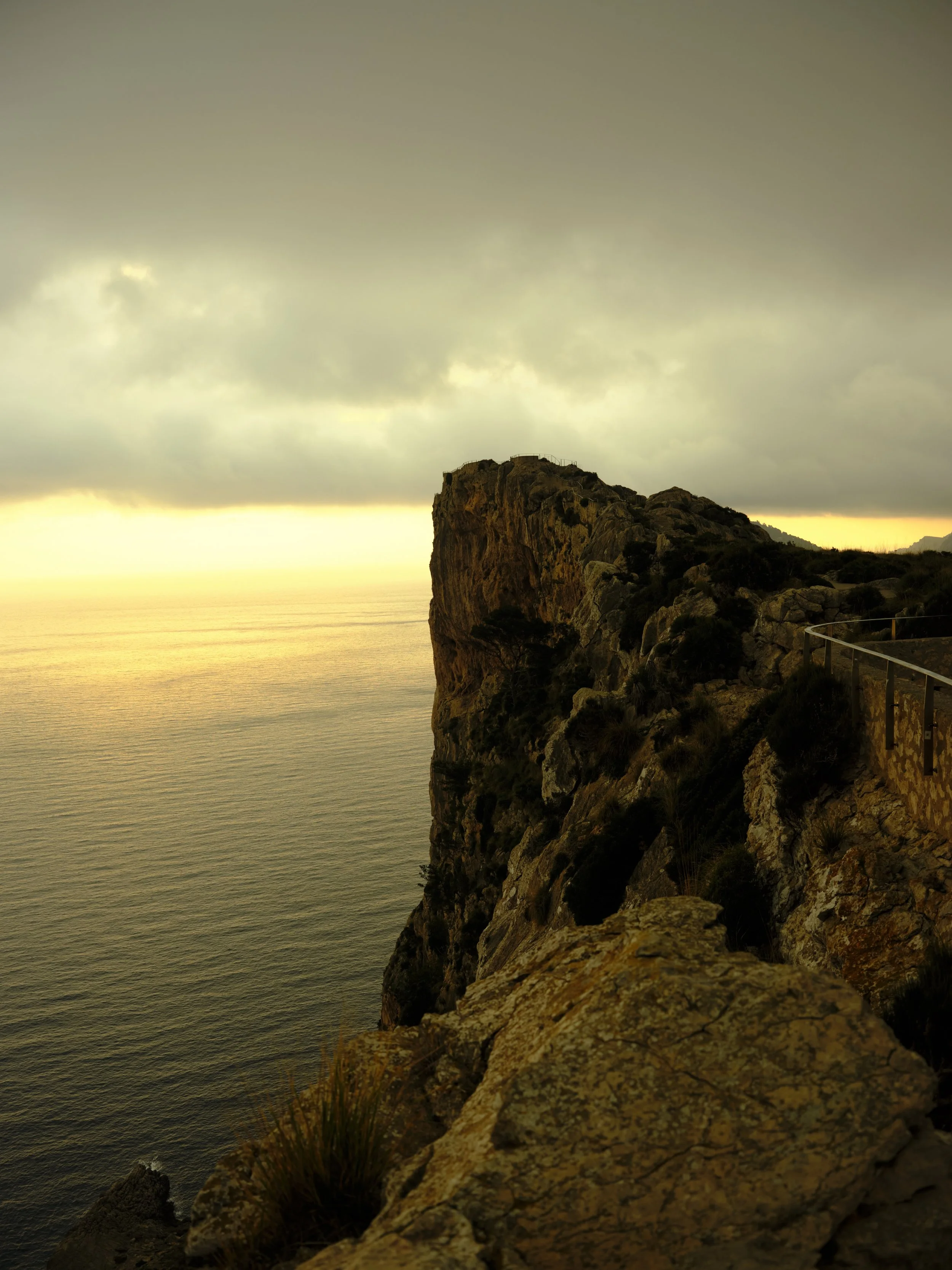 Een rotsformatie langs een afgezet wandelpad in Mallorca met uitzicht op de oceaan bij zonsondergang onder bewolkte hemel gefotografeerd door Eric van den Elsen.