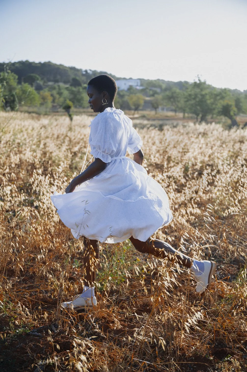 Een vrouw in een witte jurk rent door een veld met dorre, bruine planten op een zonnige dag gefotografeerd door Eric van den Elsen.