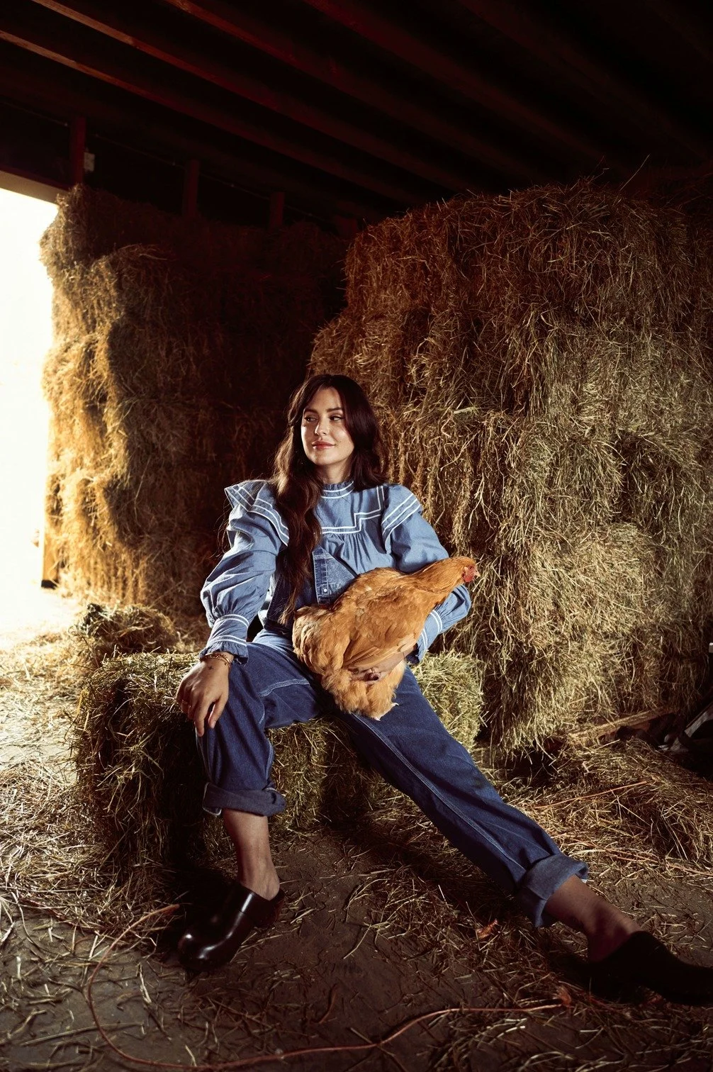 Romy Boomsma zit op een hooibal in een schuur met een kip op haar schoot gefotografeerd door Eric van den Elsen.