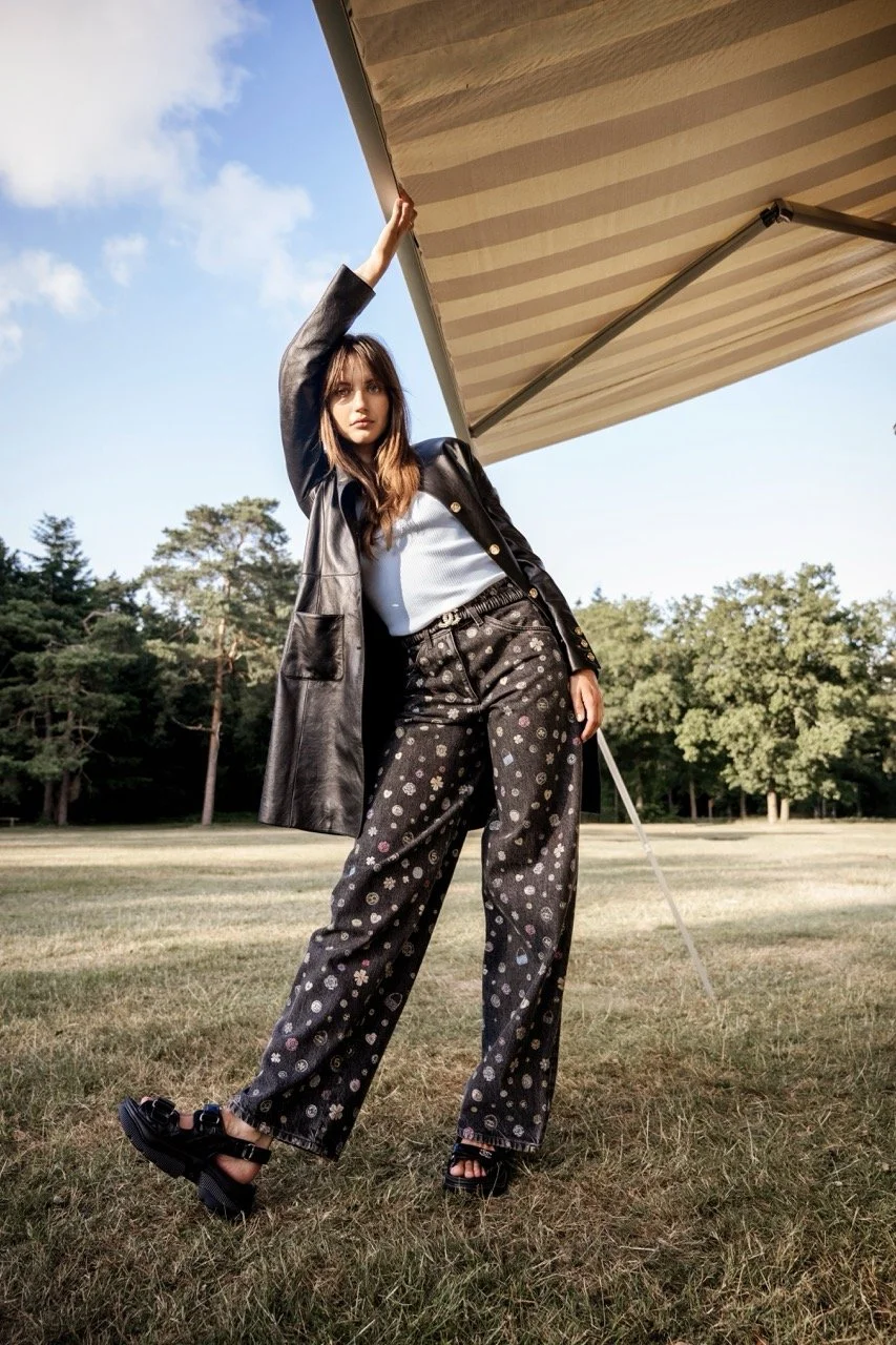 Een jonge vrouw staat op een grasveld onder een grote parasoldoek met een blauwachtige hemel en enkele bomen op de achtergrond gefotografeerd door Eric van den Elsen.