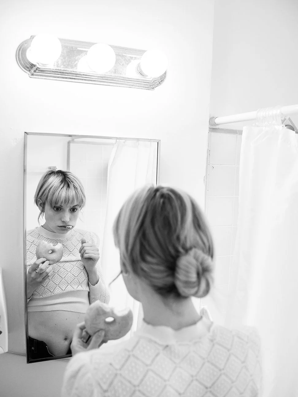 Een vrouw kijkt in de spiegel terwijl ze een appel met een stuk ontbreekt vasthoudt gefotografeerd door Eric van den Elsen.