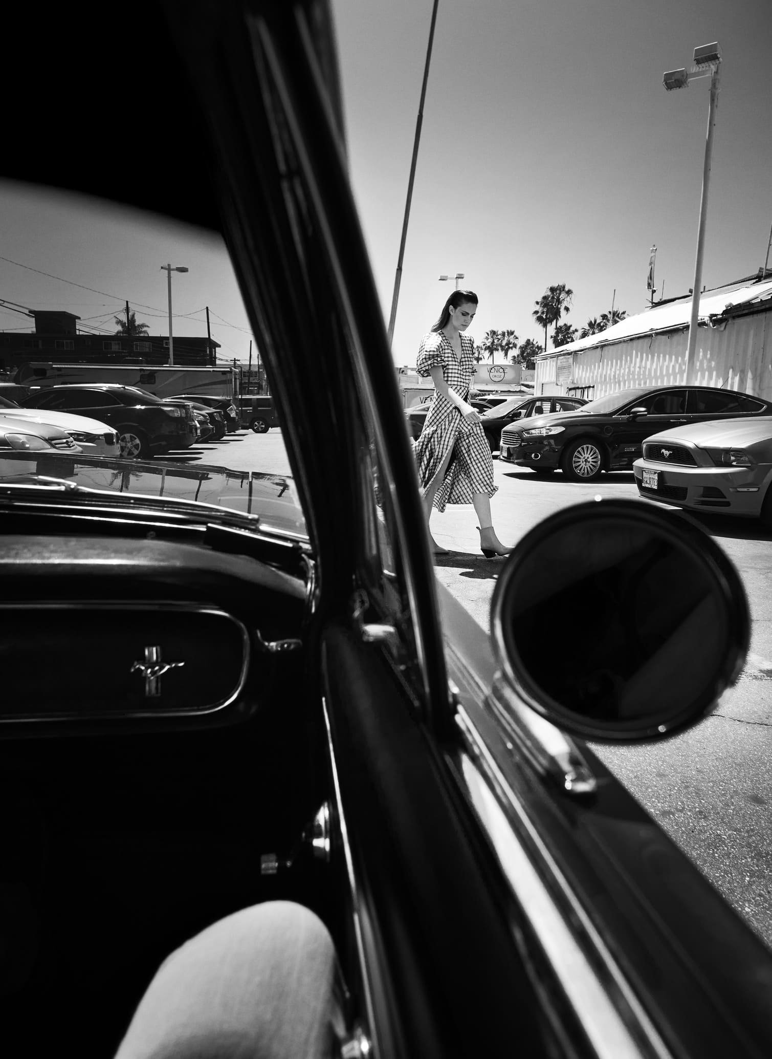 Zwarte en witte foto van een autointerieur, met een vrouw die over de parkeerplaats loopt, gezien door het raam van de auto gefotografeerd door Eric van den Elsen.