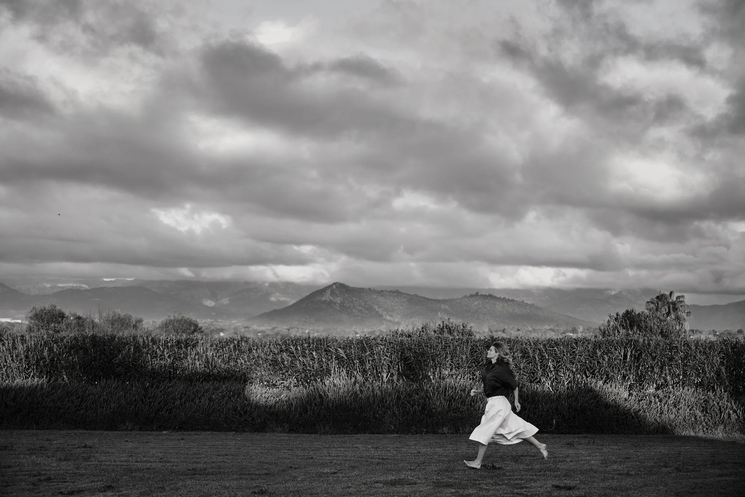 Een model in de voorgrond lopend door het veld met een cinematische natuurlandschap op de achtergrond gefotografeerd door Eric van den Elsen voor Josephine & Co.