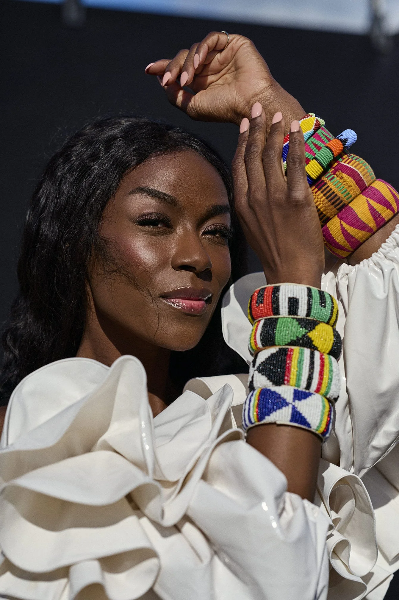 Close-up van Giovanca Ostiana met donkere huid die sieraden met kleurrijke Afrikaanse patronen draagt en een witte outfit met grote ruches gefotografeerd door Eric van den Elsen.