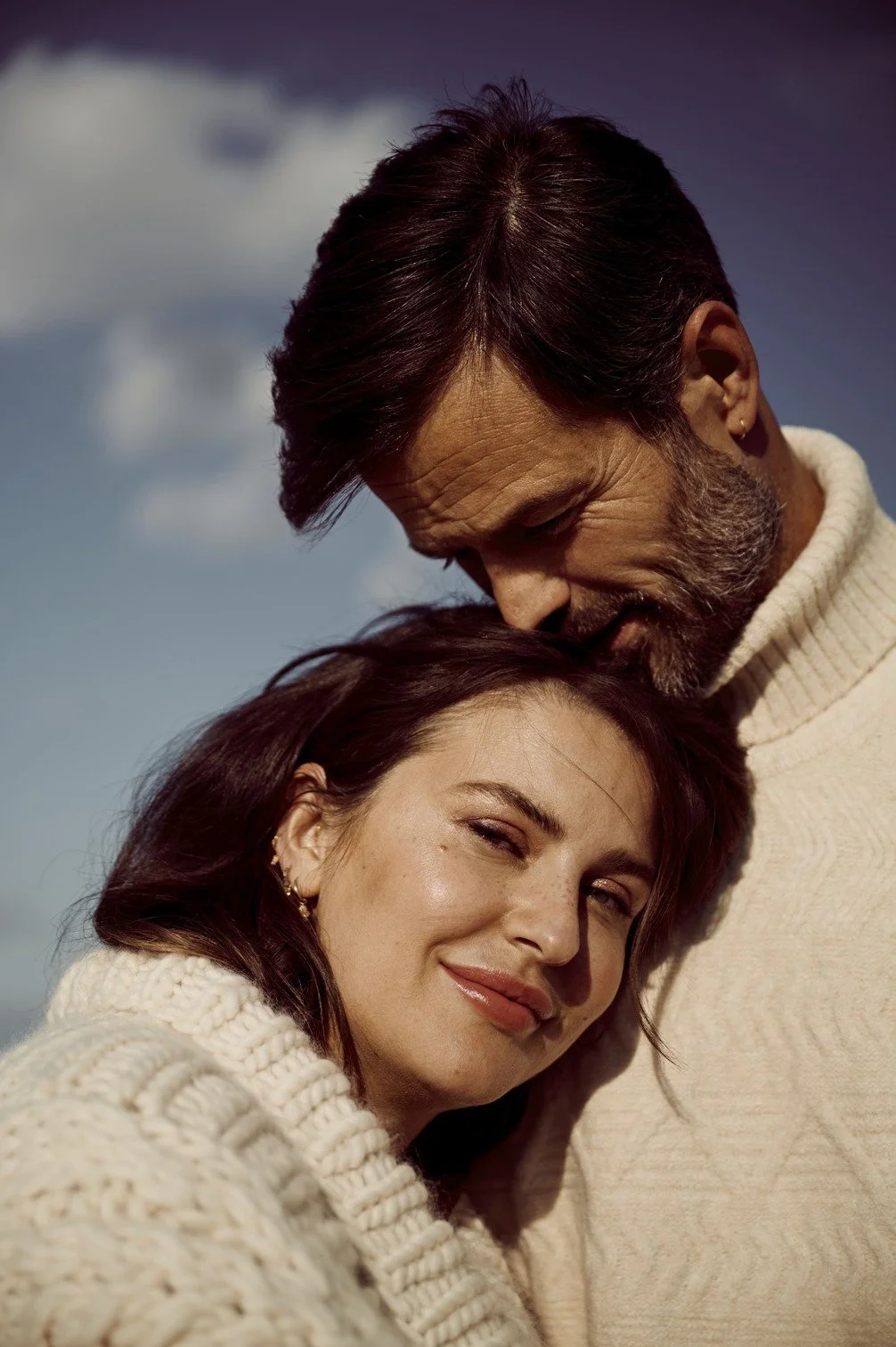 Arie en Romy Boomsma in een warme omhelzing, beiden dragen dikke witte truien, ze staan buiten onder een bewolkte hemel gefotografeerd door Eric van den Elsen.