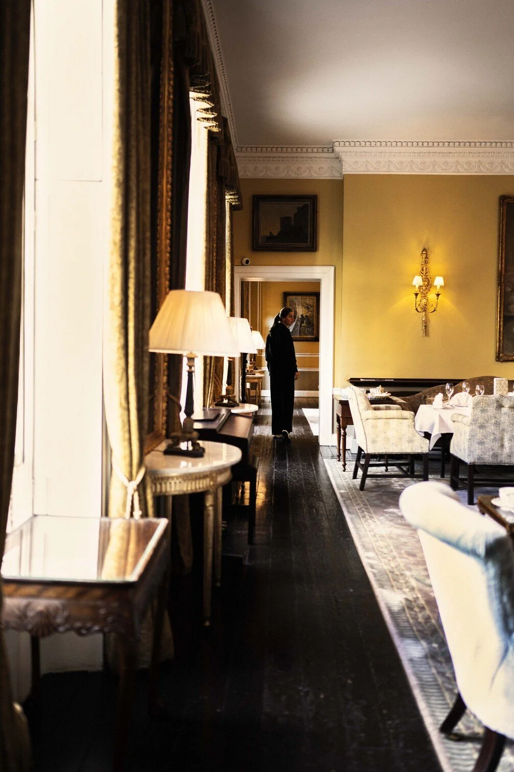 Een elegant restaurantinterieur met geelgekleurde muren, versierd met wandlampen en kunstwerken gefotografeerd door Eric van den Elsen voor Vogue Living in Ierland.