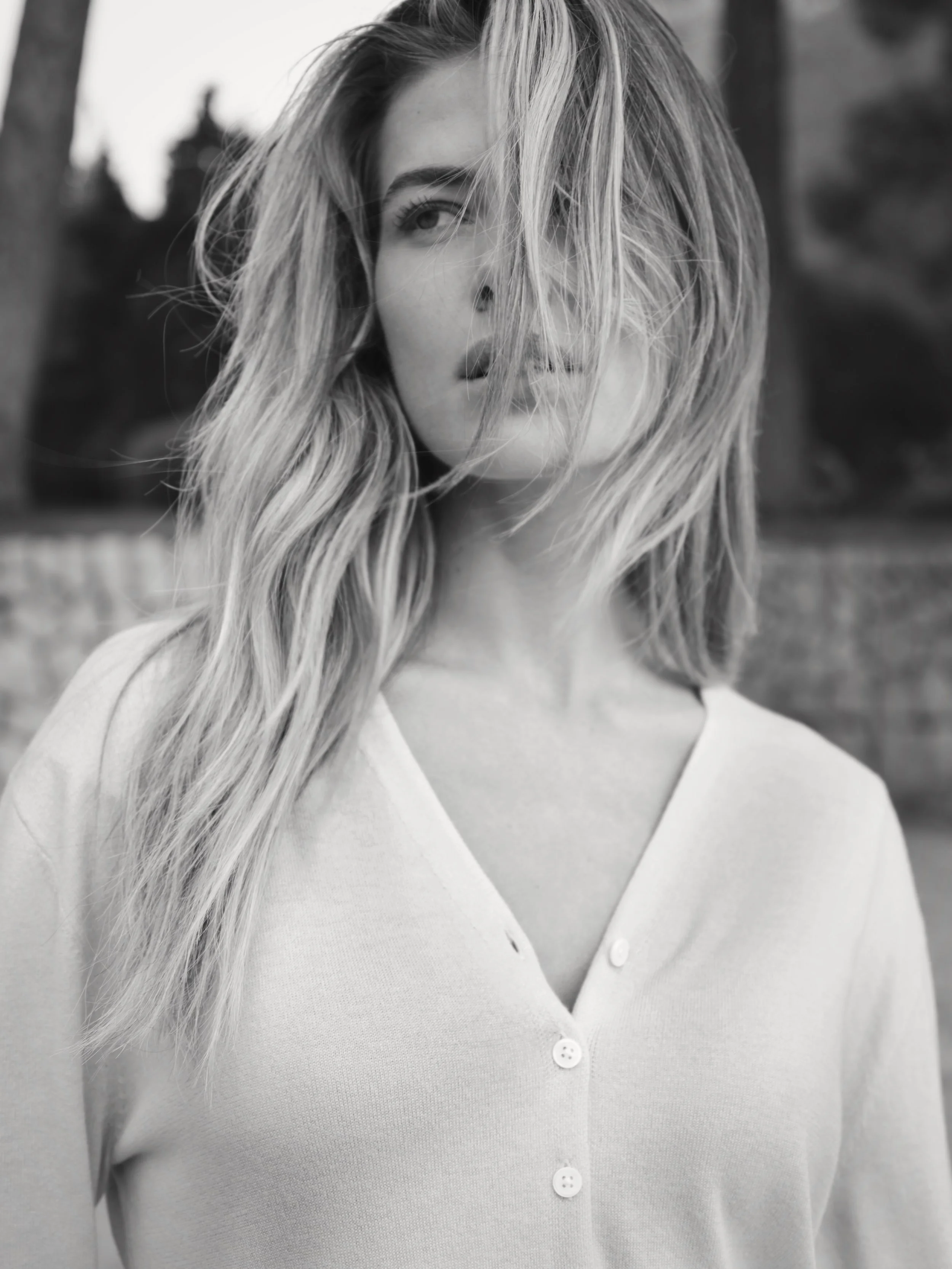 Zwart-wit foto van een vrouw met golvend haar die deels haar gezicht bedekt, met een natuurlijke achtergrond gefotografeerd door Eric van den Elsen voor Josephine & Co.