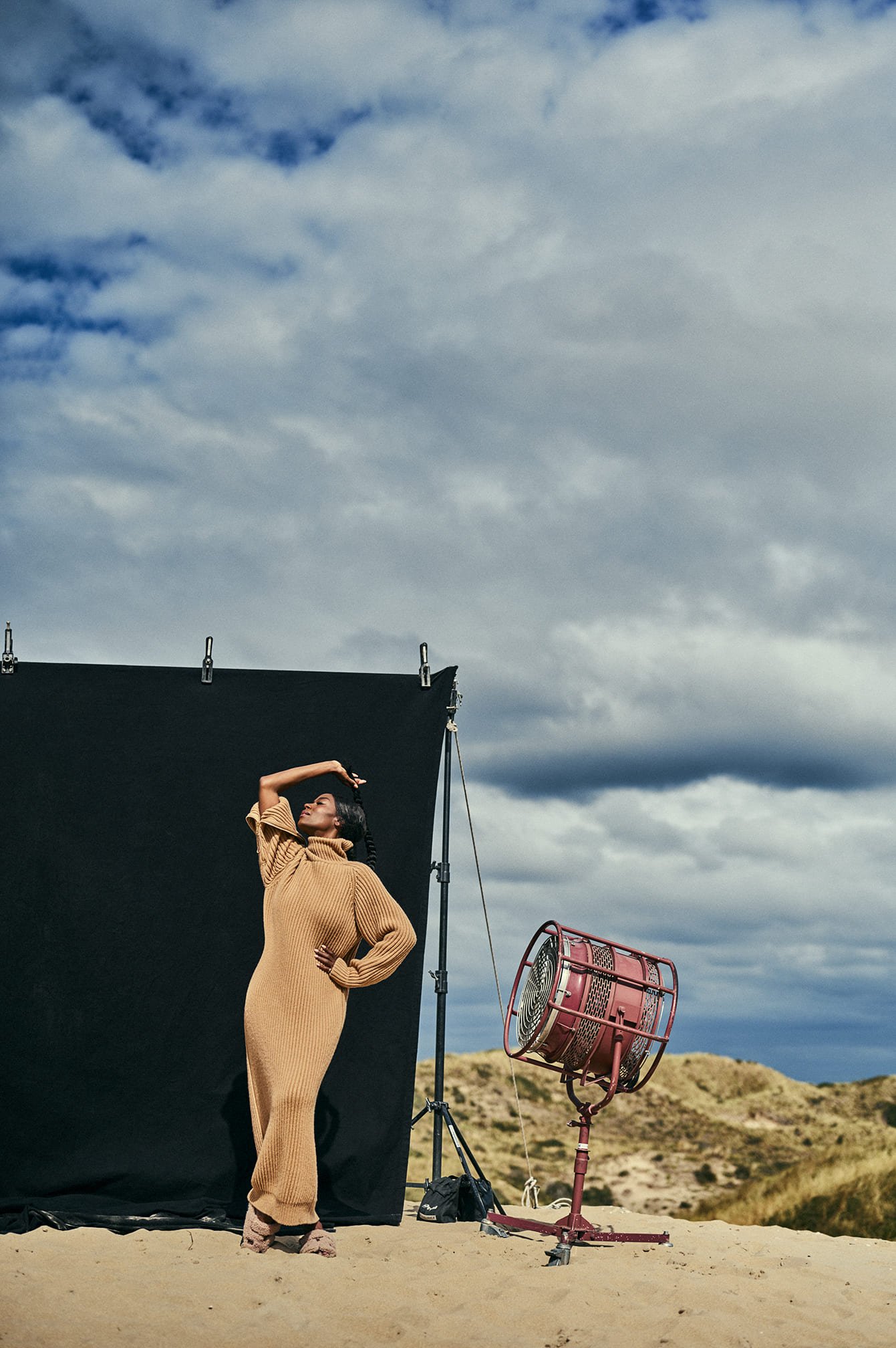 Giovanca Ostiana poseert in een golvende, caramelkleurige jurk voor een fotoshoot op een zandlandschap, met een zwart achtergronddoek en studioverlichting gefotografeerd door Eric van den Elsen.