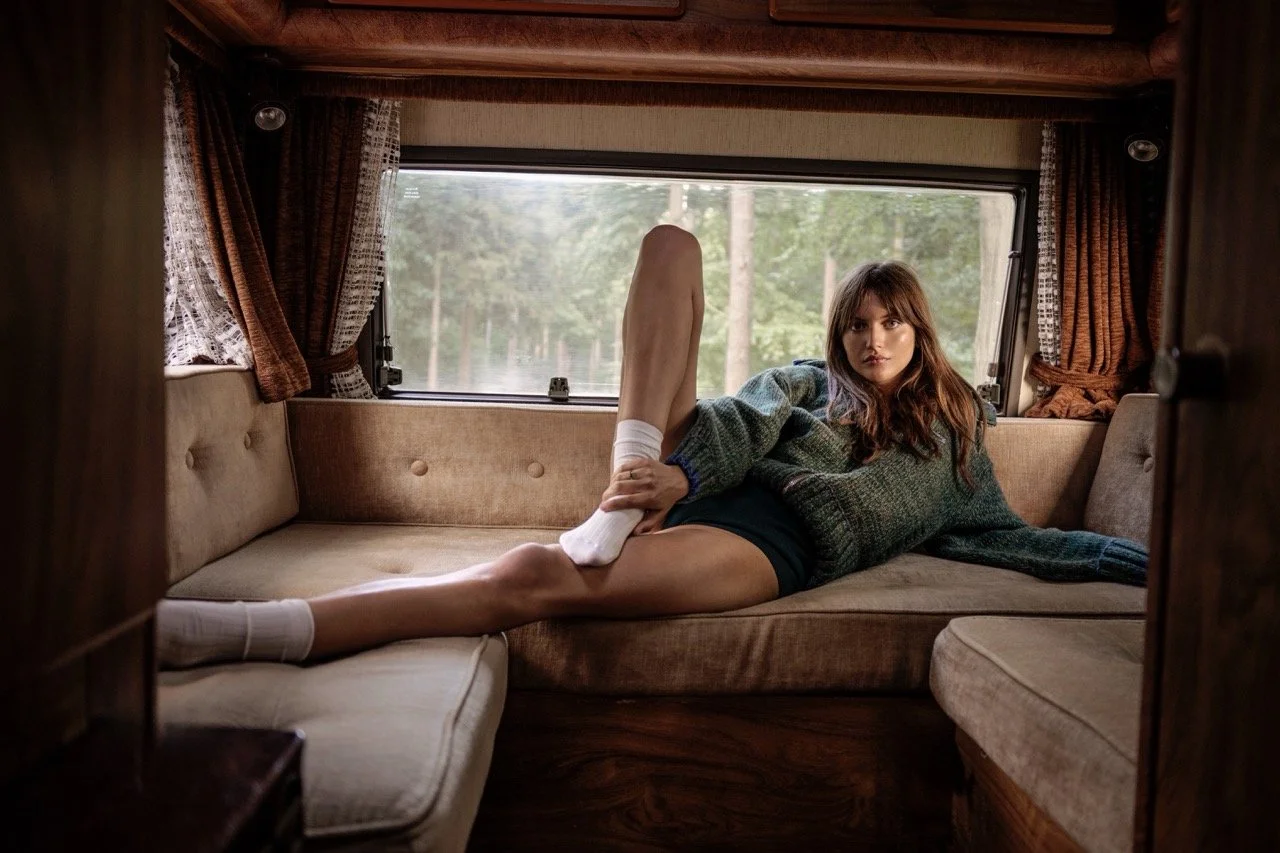 Een jonge vrouw ligt in een knusse camper, met een bos buiten het raam gefotografeerd door Eric van den Elsen.