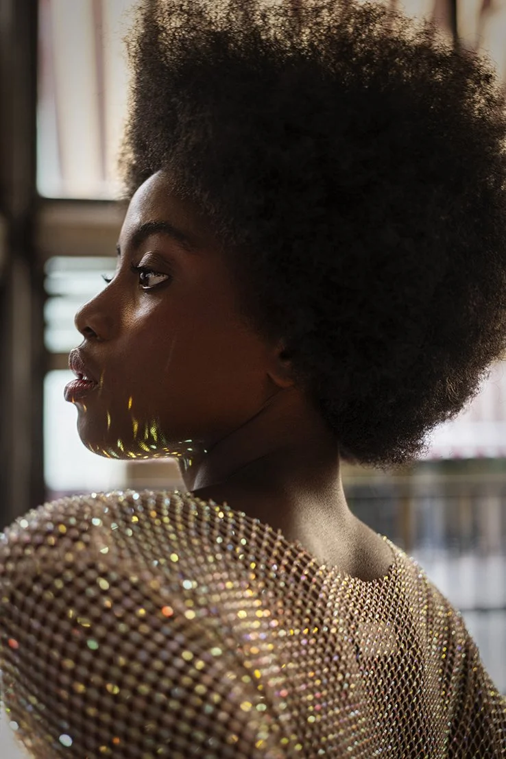 Close-up van een vrouwelijke vrouw met een grote, krullende haardos en een glanzende, gepailleerde gouden jurk gefotografeerd door Eric van den Elsen.