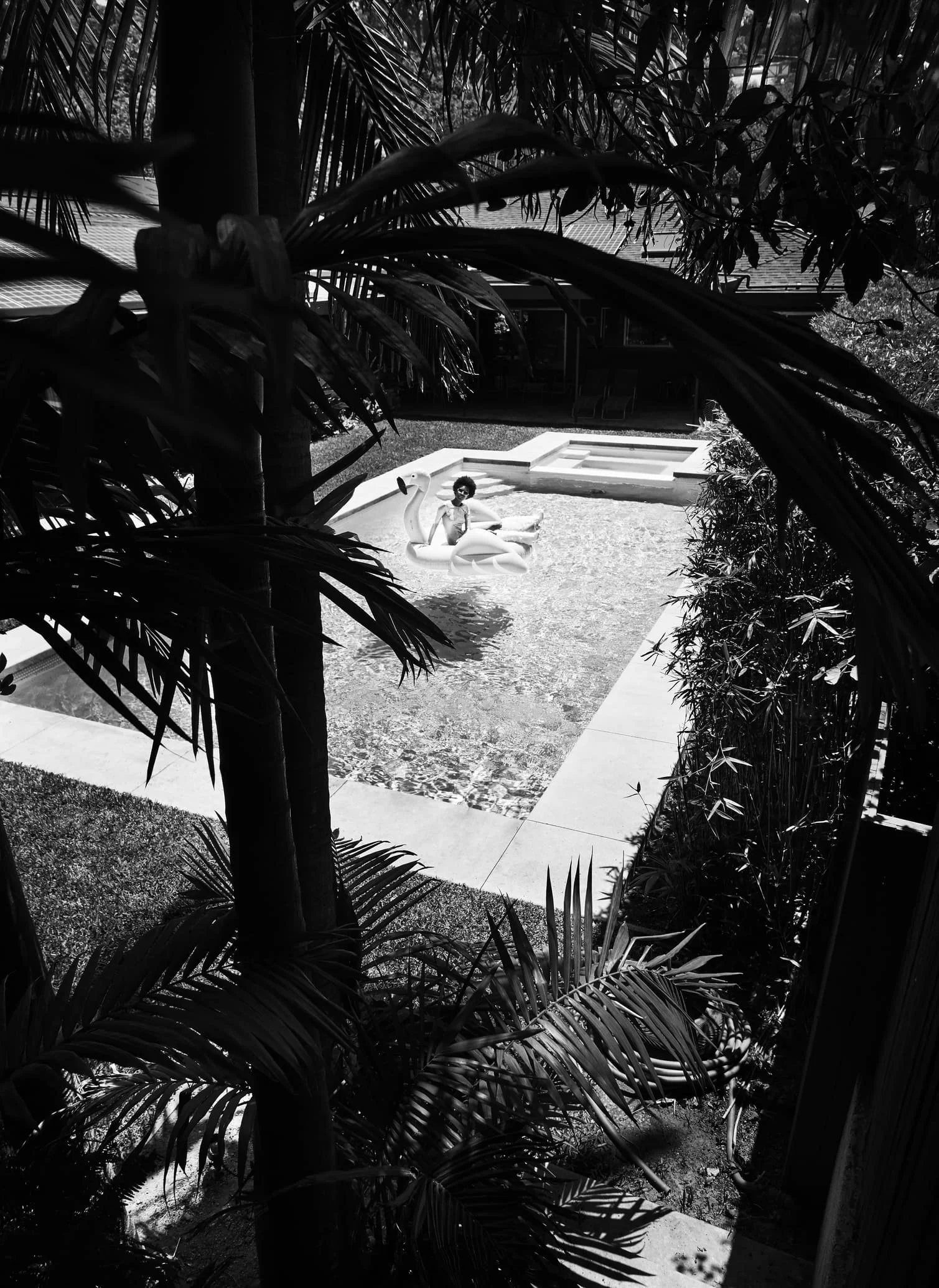 Zwart-wit foto van een terras met een zwembad, waar een persoon op een zwemband in de vorm van een zwaan ligt gefotografeerd door Eric van den Elsen.