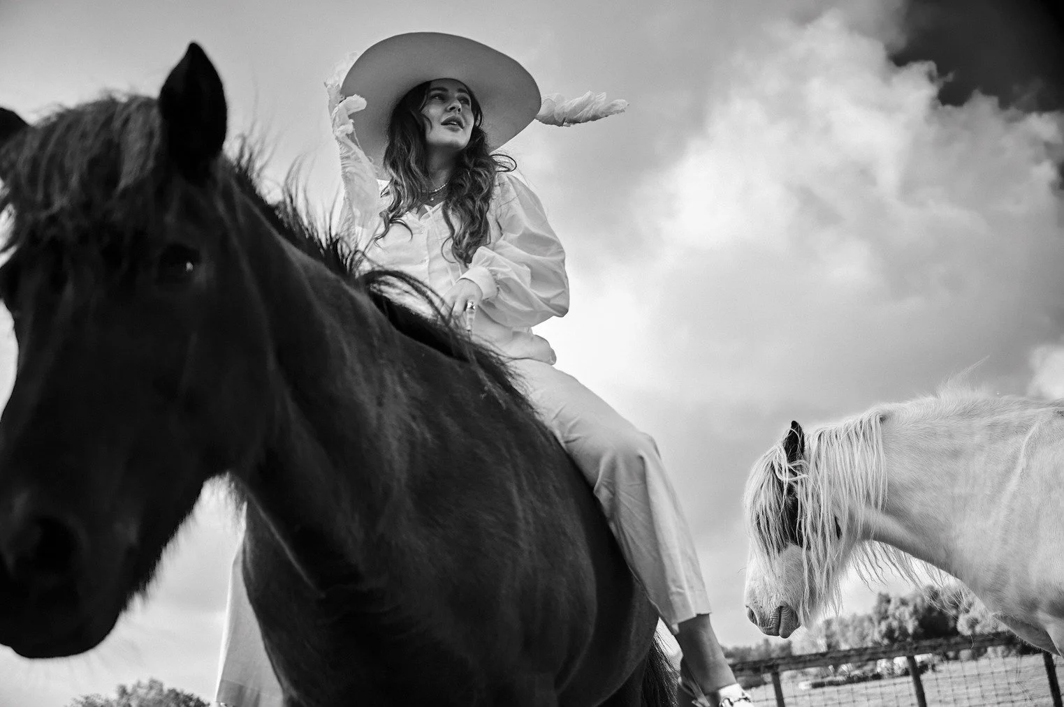 Romy Boomsma op een paard met een grote hoed, andere paarden op de achtergrond, in een open landschap gefotografeerd door Eric van den Elsen.