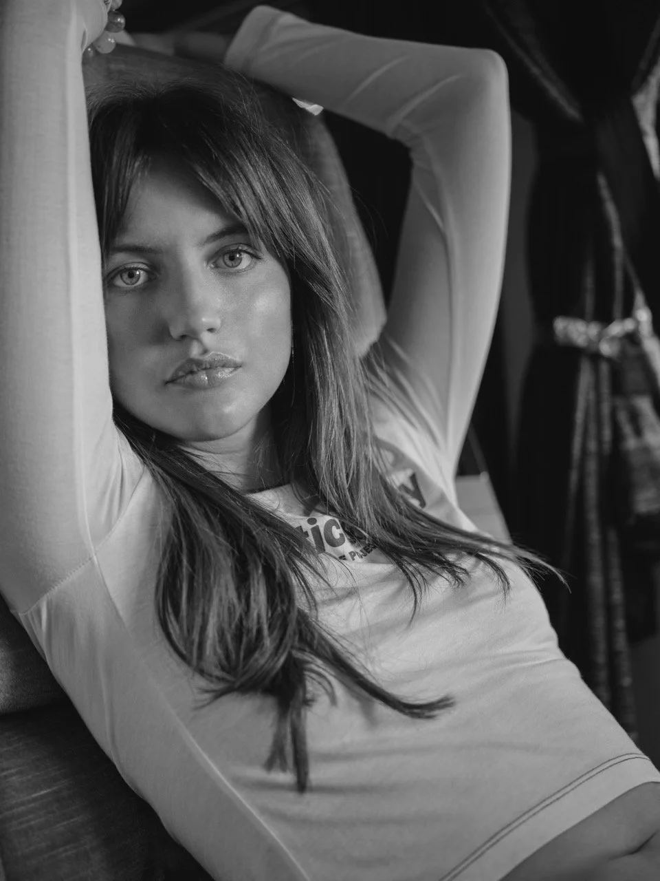 Zwart-wit foto van een vrouw liggend op een bank met haar armen omhoog, haar haar over haar schouder en direct kijkend naar de camera gefotografeerd door Eric van den Elsen.