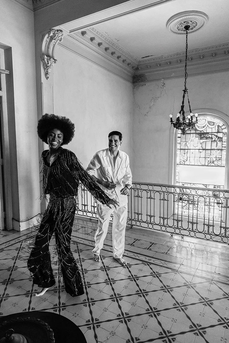 Twee mensen dansen vrolijk in een oude, sierlijke kamer met een grote raam en een kristallen kroonluchter gefotografeerd door Eric van den Elsen.